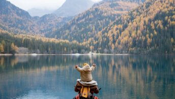 Back View of a Person Carrying a Baby near the Placid Lake Scenery